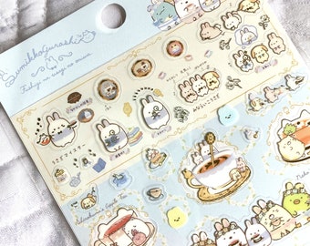 May include: A sheet of colorful stickers featuring characters from the Sumikko Gurashi series. The stickers are on a blue background with white borders and feature various characters, including a rabbit, a penguin, a bear, and a cat. The stickers are all in different poses and have different expressions. The text on the sheet reads "Sumikko Gurashi" and "Fushigi na usagi no oniwa."
