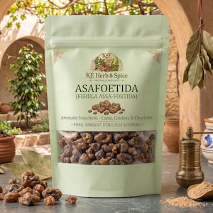 May include: A light green stand-up pouch of KE Herb & Spice Asafoetida (Ferula Assa-Foetida) with a clear window showing brown resin chunks. The label text reads Aromatic Selections - Cures, Cuisines & Character - Pure, Vibrant, Ethically Sourced.