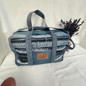 Peut inclure: Un sac de voyage rectangulaire en jean avec un motif patchwork composé de bandes de tissu bleu clair et bleu foncé. Le sac possède deux poignées supérieures, une fermeture éclair et un écusson en cuir marron avec le texte BLUE BENCH MARKET.