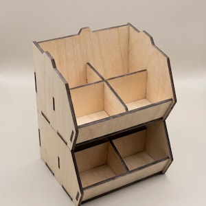 May include: A two-tiered wooden storage organizer featuring a light tan natural wood finish with dark brown edges. The unit is divided into four open compartments on the top level and two open compartments on the bottom level for storage.