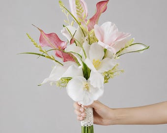 Puede incluir: Un ramo de flores que incluye calas blancas, calas con puntas rosadas, orquídeas blancas y tulipanes de color rosa pálido. Los tallos están agrupados y envueltos en una cinta de encaje blanco con detalles perlados, creando un arreglo estructurado.