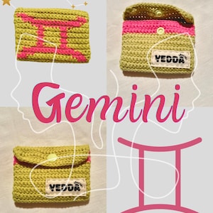 May include: A handmade olive green crochet pouch featuring a bright pink Gemini zodiac symbol on the front. The pouch includes a flap with a yellow snap button closure and a white fabric label stitched on the front that reads YEDDA CROCHET.