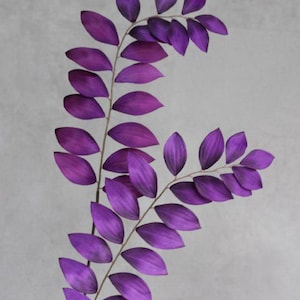 May include: Two stems of artificial ruscus foliage featuring vibrant purple oval-shaped leaves arranged in an alternating pattern along thin, flexible branches. The deep violet color is consistent across all foliage, creating a bold botanical display.