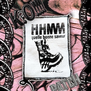 Peut inclure: Un écusson rectangulaire en tissu blanc avec une impression graphique noire représentant une botte montante à boucles. Le texte HHMM et quelle bonne saveur est imprimé au-dessus de la botte. L'écusson mesure 12cm par 8cm et a un bord cousu.