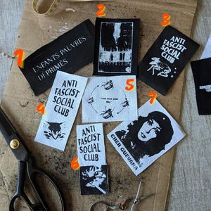 Peut inclure: Un ensemble de sept écussons en tissu rectangulaires avec des impressions graphiques en noir et blanc, incluant des textes comme ENFANTS PAUVRES DÉPRIMÉS, ANTI FASCIST SOCIAL CLUB et CHER GUEVARA, ainsi que des illustrations d'insectes et un portrait.