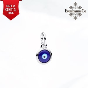 Puede incluir: Un dije de tono plateado con un diseño circular de ojo turco que presenta un centro azul oscuro, un iris azul claro y una pupila blanca. El dije incluye una pequeña argolla plateada en la parte superior. El texto EvercharmsCo es visible en la esquina.