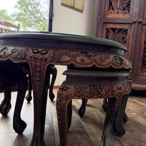 May include: A dark brown, intricately carved wooden table with a round top and detailed relief carvings. The table features ornate legs and a green felt surface. The carvings depict faces and architectural elements.