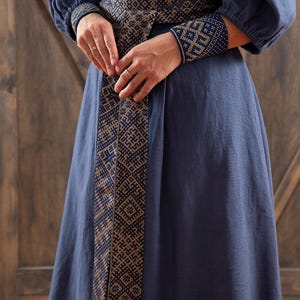 May include: A long, navy blue dress with a gold and blue patterned belt and matching wrist cuffs. The dress is made of a linen fabric.