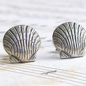May include: A pair of silver shell-shaped stud earrings. The earrings are detailed with a textured design.