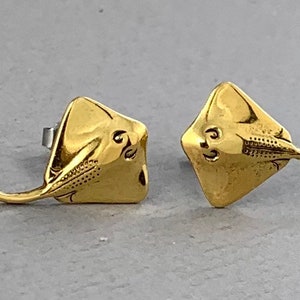 Puede incluir: Un par de pendientes de color dorado en forma de raya. Los pendientes están detallados con líneas texturizadas y un diseño en relieve.