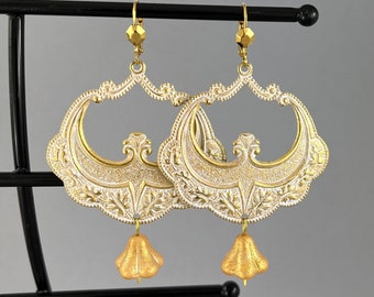 May include: A pair of gold and white filigree earrings with bell-shaped charms. The earrings are ornate and have a vintage style.