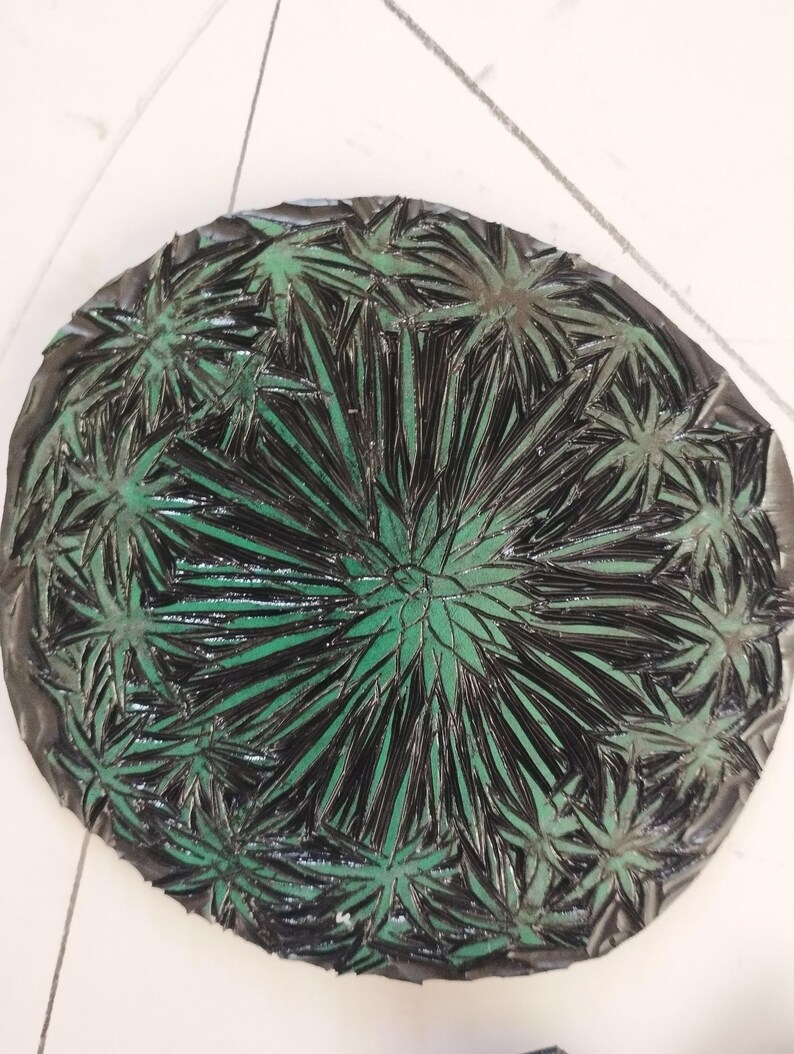 Pu&ograve; includere: Un piatto decorativo circolare caratterizzato da un motivo a raggiera in nero scuro e verde brillante. Il design &egrave; composto da numerose forme radianti e appuntite simili a foglie che si estendono dal centro verso il bordo esterno in modo denso.