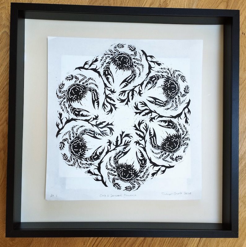 May include: A black and white linocut print featuring a circular mandala pattern of six crabs intertwined with seaweed. The artwork is presented in a square black frame with a white mount. The text "Crab & Seaweed Mandala" is printed at the bottom.