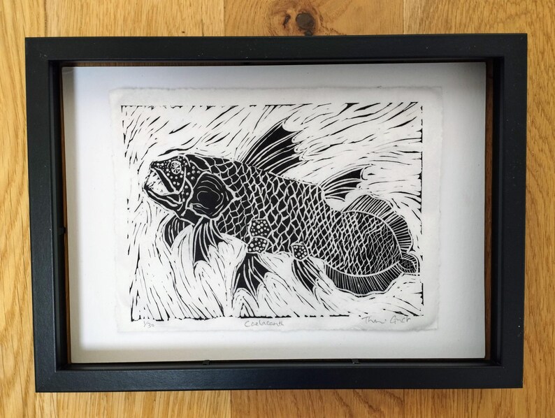Black and white relief print of a coelacanth fish swimming through textured water marks. 
Printed on hand torn deckle edged Wenzhou paper. Features detailed scales, lobed fins, and hand-penciled signature and edition details along the bottom margin. Displayed in a black frame