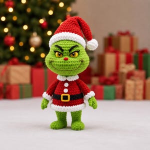 May include: A crocheted green creature doll wearing a red and white Santa hat and a matching red coat with a black belt, a yellow buckle, and two white buttons. The doll has yellow eyes, a small red nose, and a wide, thin, stitched-on smile.