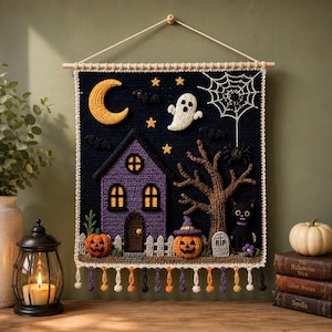 May include: A rectangular crochet wall hanging featuring a dark blue night sky with a yellow crescent moon, stars, a white ghost, and a spider web. Below, a purple house, a brown tree, two jack-o'-lanterns, a black cat, and a tombstone.
