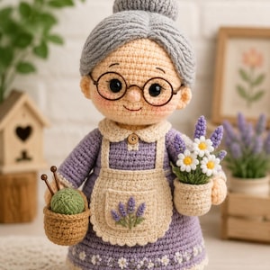 May include: A crocheted doll of an elderly person with gray hair in a bun, wearing round glasses and a purple dress with a cream-colored apron. The doll holds a small basket with green yarn and knitting needles in one hand and a pot of flowers in the other.