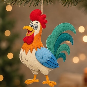 May include: A felt rooster ornament featuring a bright red comb and wattle, an orange neck, a white body, light blue wings, and a dark teal tail. The rooster has yellow feet and is suspended by a thin twine string for hanging on a tree branch.