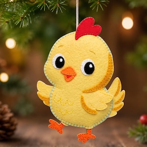 May include: A yellow felt chick ornament featuring a bright red comb, an orange beak, and large black eyes. The chick has stitched details along its edges, small orange feet, and is suspended by a thin string for hanging as a decoration.