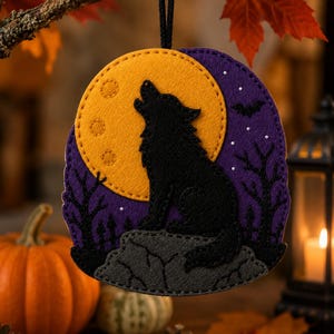 May include: A felt ornament featuring a black wolf silhouette howling at a large yellow moon against a purple night sky. The scene includes a gray rock, black tree silhouettes, and a small bat. It hangs from a black cord for display.