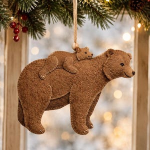 May include: A brown felt hanging ornament featuring a large bear with a smaller bear cub resting on its back. The ornament is constructed from layered brown felt with visible stitched detailing along the edges and surface, suspended by a jute twine loop.