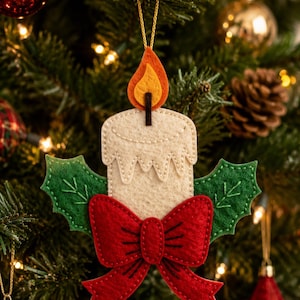 May include: A felt Christmas tree ornament shaped like a cream-colored candle with a yellow and orange flame. The candle is decorated with two green felt holly leaves and a large red felt bow at the base, all attached with visible stitching.