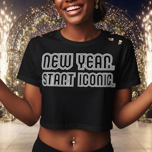 Könnte beinhalten: Ein schwarzes, kurzärmeliges bauchfreies Oberteil mit dem weißen Schriftzug NEW YEAR. START ICONIC. in einer fetten, umrandeten Schrift auf der Brust. Das Kleidungsstück hat einen einfachen Rundhalsausschnitt und einen geraden Saum.