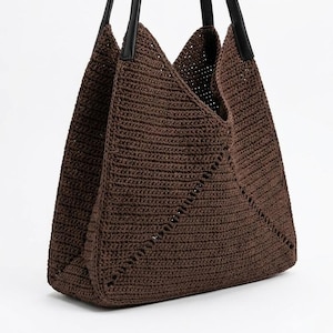May include: A dark brown crochet tote bag featuring a structured triangular silhouette with a textured knit pattern and two long, smooth black handles attached to the top edges of the bag, creating a distinct V-shaped opening at the center.