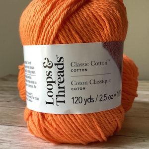 May include: A ball of bright orange yarn with a white paper label reading Loops & Threads Classic Cotton, 120 yds / 2.5 oz. The yarn is wound into a round shape, displaying a textured, twisted fiber construction in a vibrant, solid orange color.