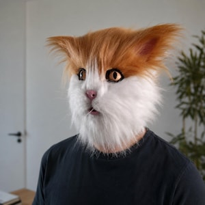 May include: A realistic cat mask featuring long, soft faux fur in shades of ginger orange and white. The mask has large, amber-colored eyes, a small pink nose, and a slightly open mouth, covering the entire head with detailed feline features.