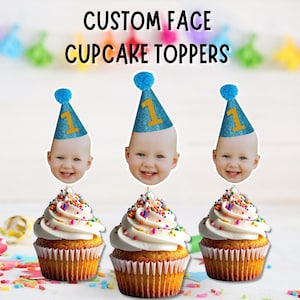Puede incluir: Tres cupcakes con glaseado blanco y chispas de colores, cada uno coronado con un recorte personalizado de la cara de un bebé con un sombrero de fiesta azul brillante con el número 1. El texto CUSTOM FACE CUPCAKE TOPPERS aparece arriba.