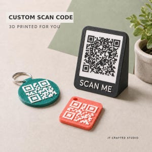 May include: A black 3D printed stand with a white QR code and the text SCAN ME, a round green keychain with a white QR code, and a square red keychain with a white QR code. The text CUSTOM SCAN CODE 3D PRINTED FOR YOU is visible.