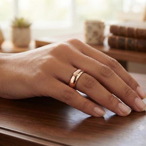 Könnte beinhalten: Ein polierter Ring aus Roségold mit einer glatten, abgerundeten Oberfläche und einem hochglänzenden Finish. Der Ring zeichnet sich durch eine einfache, massive Konstruktion mit gleichbleibender Breite aus und zeigt einen warmen Metallton.