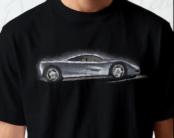 Pode incluir: Uma t-shirt preta de manga curta com uma ilustração estilizada e pictórica de um carro desportivo prateado de perfil. O gráfico do carro é apresentado num estilo de pinceladas suaves com reflexos brancos, centrado na zona do peito.