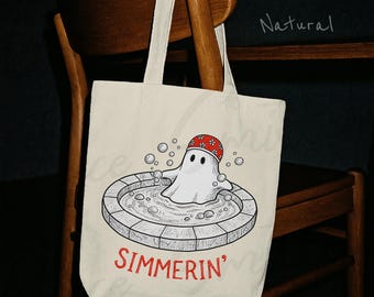 Pode incluir: Uma sacola de lona na cor natural com uma ilustração gráfica de um fantasma branco usando uma touca de banho vermelha com estampa floral, sentado em uma banheira redonda cheia de bolhas. O texto "SIMMERIN'" está impresso em vermelho.