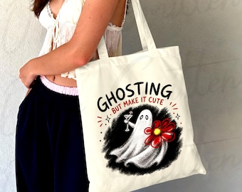 Pode incluir: Uma sacola de lona cor de creme com um gráfico de um fantasma branco segurando uma taça de martini e uma flor vermelha grande. O texto acima do fantasma diz GHOSTING BUT MAKE IT CUTE em letras pretas e vermelhas sobre um fundo cinza.