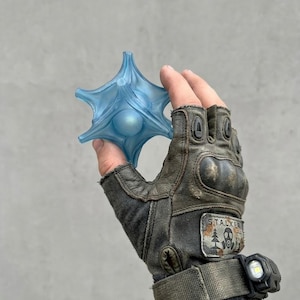 May include: A translucent light blue, star-shaped object with a central sphere, held by a finger. The object features six pointed arms extending from a rounded core. The surface has a smooth, matte finish with subtle ridges along each arm.