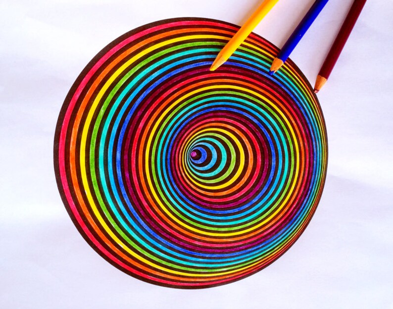 K&ouml;nnte beinhalten: Ein farbenfrohes Regenbogen-Spiralendesign, das mit Buntstiften auf wei&szlig;es Papier gezeichnet wurde. Die Stifte liegen neben der Spirale auf dem Papier.