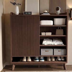 May include: A dark brown wooden storage cabinet featuring a vertical slatted sliding door on the left and open shelving on the right. The shelves contain various items including a white container, a handbag, folded white textiles, and storage boxes.