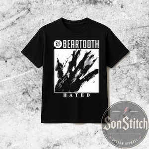 Puede incluir: Una camiseta negra de manga corta con un gráfico cuadrado blanco en el pecho. El gráfico muestra un diseño de huella de mano en tinta negra con el texto BEARTOOTH arriba y la palabra HATED impresa en letras mayúsculas blancas debajo.