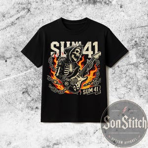 May include: A black short-sleeve t-shirt featuring a graphic print of a skeleton in a hooded cloak playing an electric guitar. The design includes orange and yellow flames, metallic chains, and the text SUM 41 printed in a bold, distressed font.