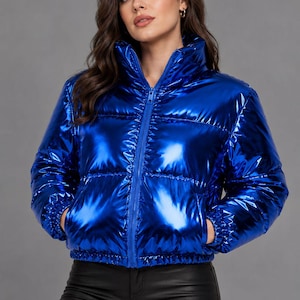 Puede incluir: Una chaqueta acolchada de color azul real vibrante con cuello alto, cremallera frontal completa y mangas largas con puños elásticos. La chaqueta presenta un acabado metálico brillante y costuras horizontales acolchadas.