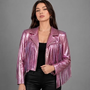 May include: A metallic pink jacket featuring a textured snakeskin pattern and long fringe detailing across the chest and sleeves. The jacket has a classic collar, long sleeves, and a cropped silhouette, worn over a simple black top.