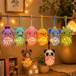 May include: A collection of eight hanging crochet animal ornaments, each featuring a spherical base illuminated by internal warm LED lights. The figures include a purple rabbit, teal bear, pink rabbit, yellow chick, blue elephant, green dinosaur, brown bear, and panda.