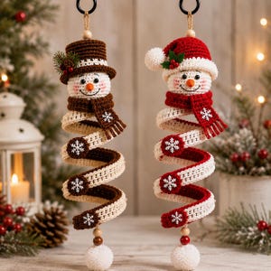 Pode incluir: Dois enfeites de boneco de neve em crochê com corpos em espiral. Um usa cartola e cachecol castanhos, o outro gorro de Pai Natal e cachecol vermelhos. Ambos apresentam pompons brancos na base e decorações de flocos de neve nos corpos.