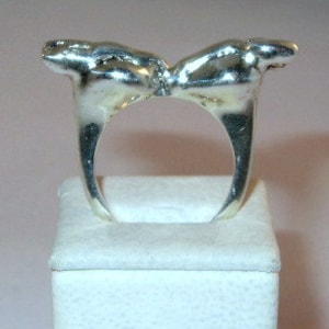 May include: A silver ring with two abstract figures facing each other, forming a heart shape.