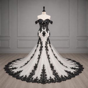Könnte beinhalten: Ein bodenlanges weißes Kleid mit schulterfreiem Ausschnitt und Meerjungfrauen-Silhouette. Das Kleid ist mit aufwendigen schwarzen Spitzenapplikationen in Blumenform verziert, die vom Oberteil bis zur breiten, ausladenden Schleppe reichen.