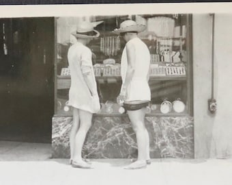 Può includere: Due persone con cappelli guardano una vetrina di gioielli in un negozio. La persona a sinistra indossa un cappello a tesa larga e un vestito bianco. La persona a destra indossa un cappello a tesa larga e una camicia bianca.