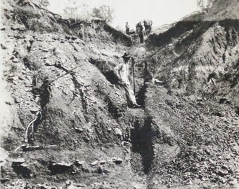 Può includere: Una fotografia in bianco e nero di una collina rocciosa e ripida con un sentiero stretto intagliato in essa. Un uomo con una camicia chiara si trova in fondo al sentiero, guardando verso l'alto. Altre figure sono visibili in lontananza, anche loro in piedi sul sentiero.