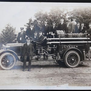 Könnte beinhalten: Ein Schwarzweiß-Foto aus der Zeit um 1900, das eine Gruppe von Männern vor einem Feuerwehrauto zeigt. Das Auto ist mit "Lynden" beschriftet und hat einen großen Schlauch hinten. Die Männer tragen Anzüge und Hüte.